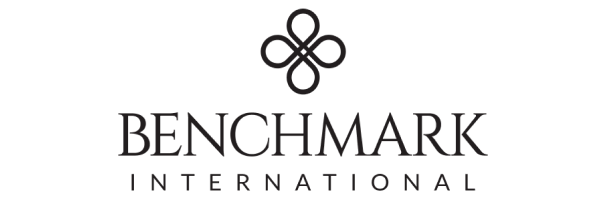 Logo for Benchmark International featuring a symmetrical, abstract geometric design above the words BENCHMARK INTERNATIONAL in uppercase, elegant black font on a light background.